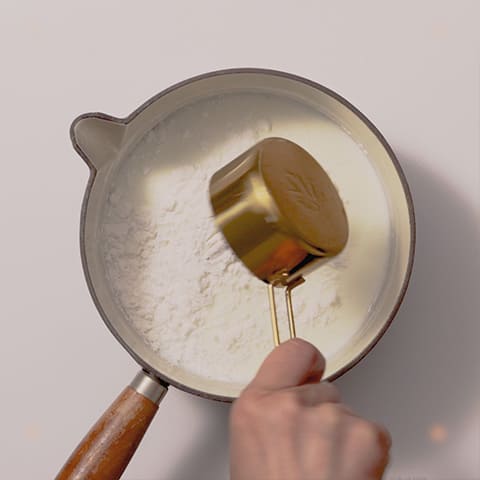 <3>の残った牛乳の鍋に米粉を加えて火にかけ、泡立て器で底から混ぜながら加熱する。